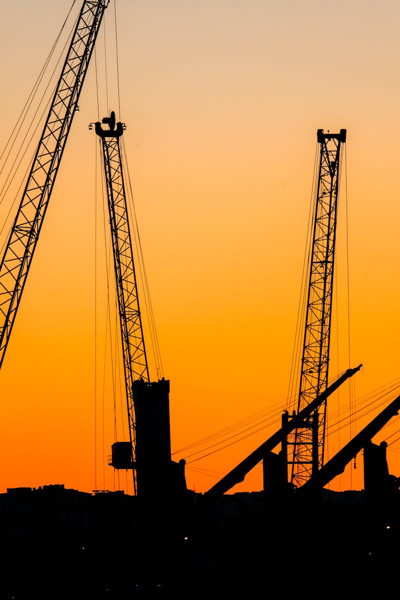 Cranes silhouetted against a colorful sunset, capturing an industrial skyline scene.